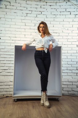 Stüdyoda beyaz gömlekli seksi ve seksi bir kadının beyaz bir duvara poz verdiği bir fotoğraf..  