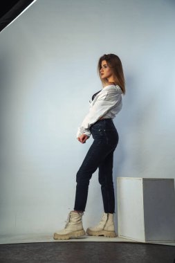 Stüdyoda beyaz bir duvara poz veren uzun saçlı seksi ve şehvetli genç bir kadının fotoğrafı..  