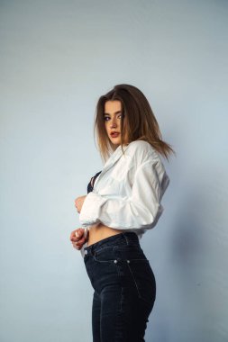 Stüdyoda beyaz bir duvara poz veren uzun saçlı seksi ve şehvetli genç bir kadının fotoğrafı..  