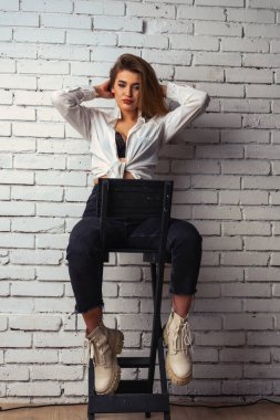 Stüdyoda beyaz gömlekli seksi ve seksi bir kadının beyaz bir duvara poz verdiği bir fotoğraf..  