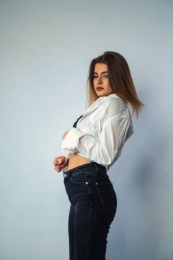Stüdyoda beyaz bir duvara poz veren uzun saçlı seksi ve şehvetli genç bir kadının fotoğrafı..  