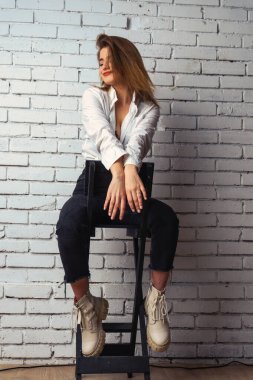 Stüdyoda beyaz gömlekli seksi ve seksi bir kadının beyaz bir duvara poz verdiği bir fotoğraf..  