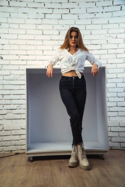 Stüdyoda beyaz gömlekli seksi ve seksi bir kadının beyaz bir duvara poz verdiği bir fotoğraf..  