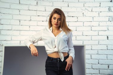 Stüdyoda beyaz gömlekli seksi ve seksi bir kadının beyaz bir duvara poz verdiği bir fotoğraf..  