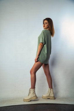 Stüdyoda beyaz bir duvara poz veren uzun saçlı seksi ve şehvetli genç bir kadının fotoğrafı..  