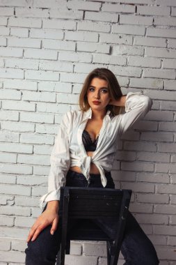 Stüdyoda beyaz gömlekli seksi ve seksi bir kadının beyaz bir duvara poz verdiği bir fotoğraf..  