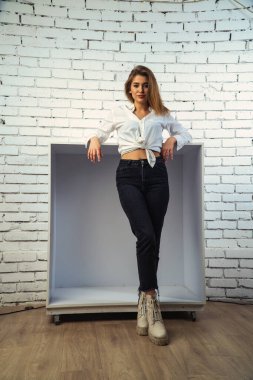 Stüdyoda beyaz gömlekli seksi ve seksi bir kadının beyaz bir duvara poz verdiği bir fotoğraf..  