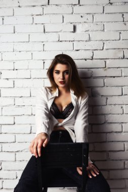 Stüdyoda beyaz gömlekli seksi ve seksi bir kadının beyaz bir duvara poz verdiği bir fotoğraf..  