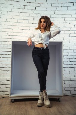 Stüdyoda beyaz gömlekli seksi ve seksi bir kadının beyaz bir duvara poz verdiği bir fotoğraf..  