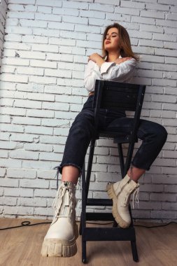 Stüdyoda beyaz gömlekli seksi ve seksi bir kadının beyaz bir duvara poz verdiği bir fotoğraf..  