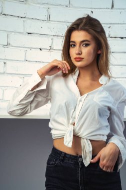 Stüdyoda beyaz gömlekli seksi ve seksi bir kadının beyaz bir duvara poz verdiği bir fotoğraf..  