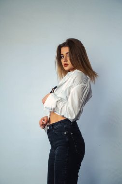 Stüdyoda beyaz bir duvara poz veren uzun saçlı seksi ve şehvetli genç bir kadının fotoğrafı..  