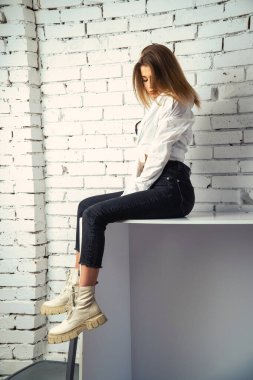 Stüdyoda beyaz gömlekli seksi ve seksi bir kadının beyaz bir duvara poz verdiği bir fotoğraf..  