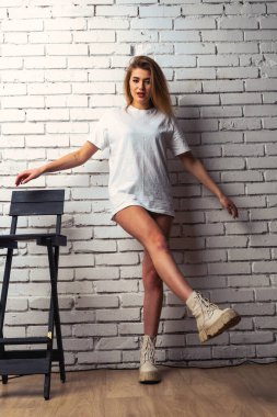 Stüdyoda beyaz bir duvara poz veren uzun saçlı seksi ve şehvetli genç bir kadının fotoğrafı..  