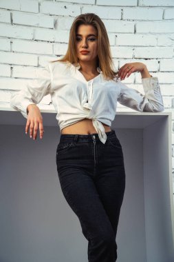 Stüdyoda beyaz gömlekli seksi ve seksi bir kadının beyaz bir duvara poz verdiği bir fotoğraf..  