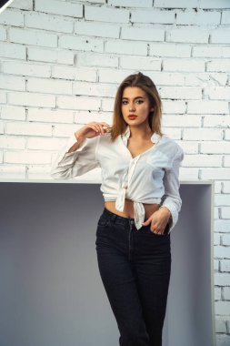 Stüdyoda beyaz gömlekli seksi ve seksi bir kadının beyaz bir duvara poz verdiği bir fotoğraf..  