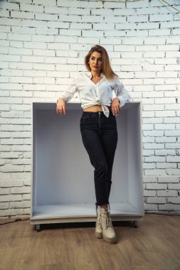 Stüdyoda beyaz gömlekli seksi ve seksi bir kadının beyaz bir duvara poz verdiği bir fotoğraf..  