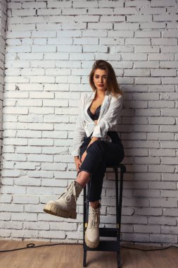 Stüdyoda beyaz gömlekli seksi ve seksi bir kadının beyaz bir duvara poz verdiği bir fotoğraf..  