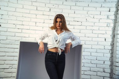 Stüdyoda beyaz gömlekli seksi ve seksi bir kadının beyaz bir duvara poz verdiği bir fotoğraf..  