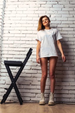 Stüdyoda beyaz bir duvara poz veren uzun saçlı seksi ve şehvetli genç bir kadının fotoğrafı..  