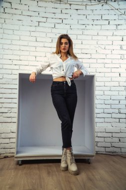 Stüdyoda beyaz gömlekli seksi ve seksi bir kadının beyaz bir duvara poz verdiği bir fotoğraf..  