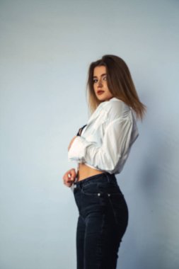 Stüdyoda beyaz bir duvara poz veren uzun saçlı seksi ve şehvetli genç bir kadının fotoğrafı..  
