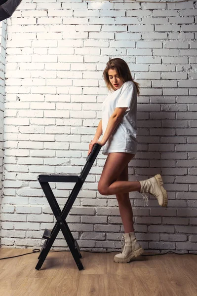 Stüdyoda beyaz bir duvara poz veren uzun saçlı seksi ve şehvetli genç bir kadının fotoğrafı..  