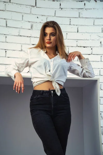 Stüdyoda beyaz gömlekli seksi ve seksi bir kadının beyaz bir duvara poz verdiği bir fotoğraf..  
