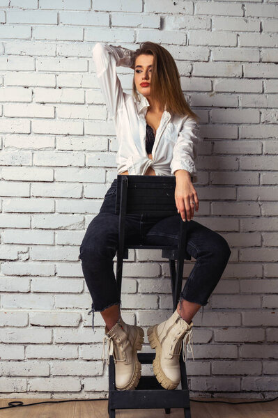 Фото молодой красивой чувственной и сексуальной женщины с длинными волосами в белой рубашке, позирующей против белой кирпичной стены в студии.  