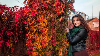 Güz parkında eşarplı genç bir kadın kameraya poz veriyor.