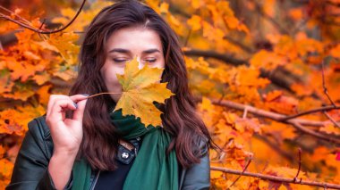 Güz parkında eşarplı genç bir kadın kameraya poz veriyor.
