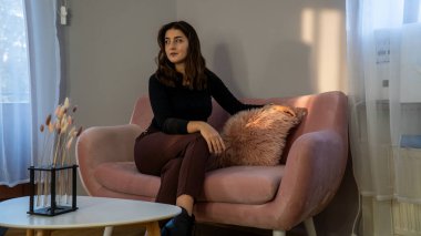 Gündelik giysiler içinde güzel bir genç kız sabahları kanepede oturuyor.