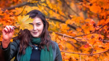 Güz parkında eşarplı genç bir kadın kameraya poz veriyor.