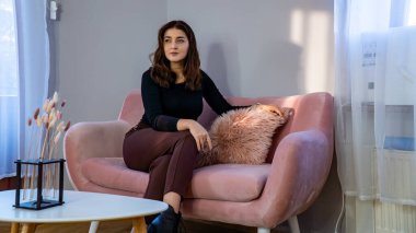 Gündelik giysiler içinde güzel bir genç kız sabahları kanepede oturuyor.