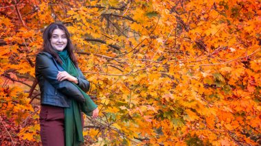 Güz parkında eşarplı genç bir kadın kameraya poz veriyor.