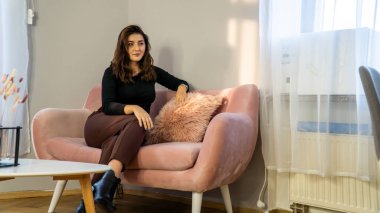 Gündelik giysiler içinde güzel bir genç kız sabahları kanepede oturuyor.