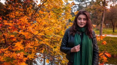 Güz parkında eşarplı genç bir kadın kameraya poz veriyor.