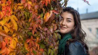 Güz parkında eşarplı genç bir kadın kameraya poz veriyor.