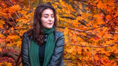 Güz parkında eşarplı genç bir kadın kameraya poz veriyor.