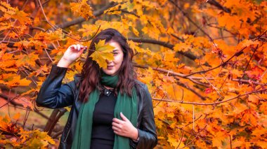 Güz parkında eşarplı genç bir kadın kameraya poz veriyor.