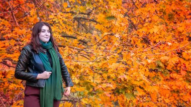 Güz parkında eşarplı genç bir kadın kameraya poz veriyor.