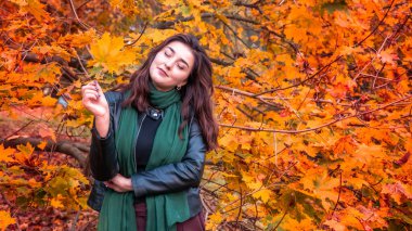 Güz parkında eşarplı genç bir kadın kameraya poz veriyor.