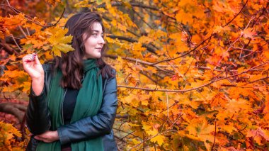 Güz parkında eşarplı genç bir kadın kameraya poz veriyor.