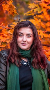 Güz parkında eşarplı genç bir kadın kameraya poz veriyor.