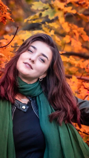 Güz parkında eşarplı genç bir kadın kameraya poz veriyor.