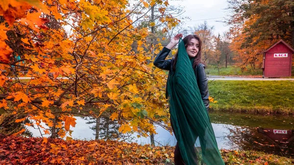 Güz parkında eşarplı genç bir kadın kameraya poz veriyor.