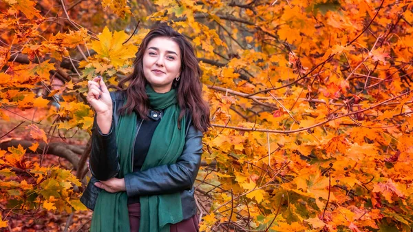 Güz parkında eşarplı genç bir kadın kameraya poz veriyor.