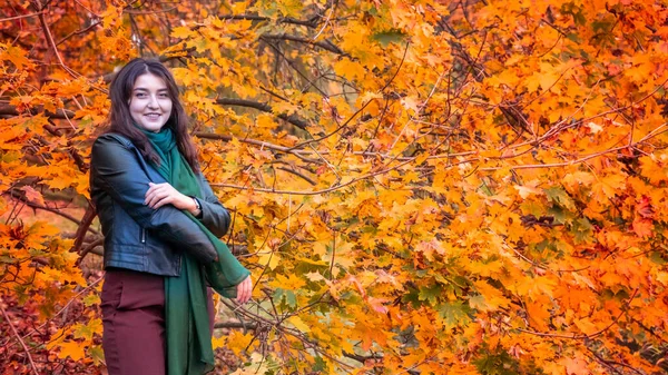 Güz parkında eşarplı genç bir kadın kameraya poz veriyor.