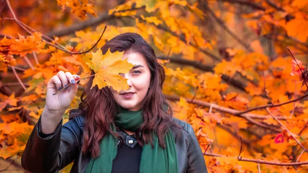 Güz parkında eşarplı genç bir kadın kameraya poz veriyor.