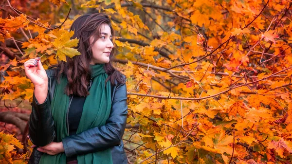 Güz parkında eşarplı genç bir kadın kameraya poz veriyor.